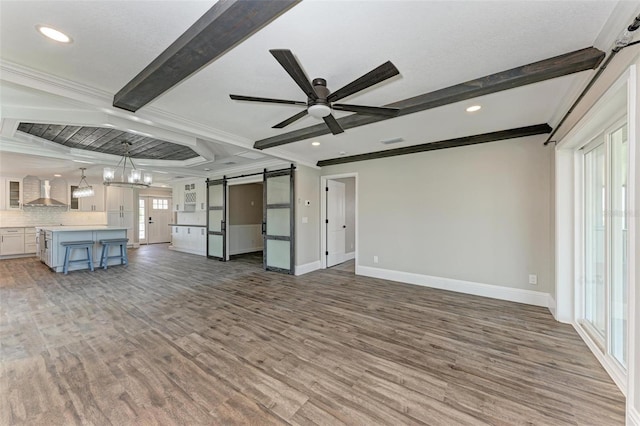 unfurnished living room featuring dark wood-type flooring, a barn door, crown molding, ceiling fan with notable chandelier, and beamed ceiling