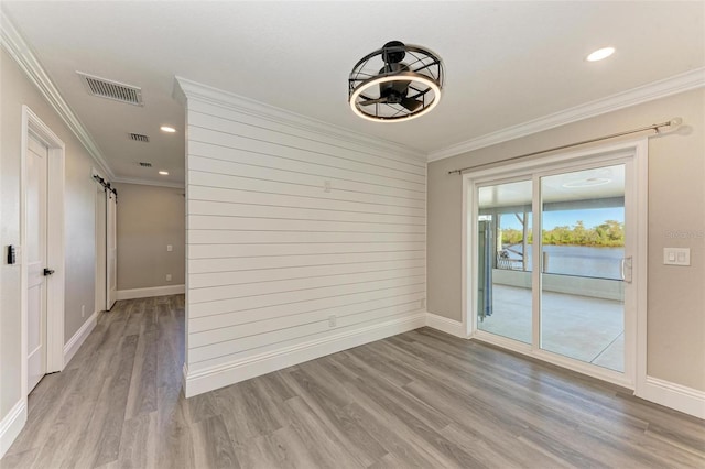 empty room with ornamental molding, light hardwood / wood-style flooring, and a barn door