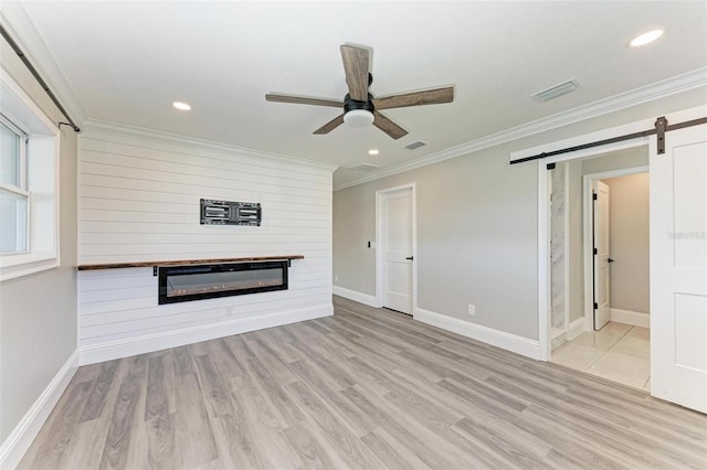 unfurnished living room featuring a barn door, light hardwood / wood-style floors, crown molding, ceiling fan, and a fireplace