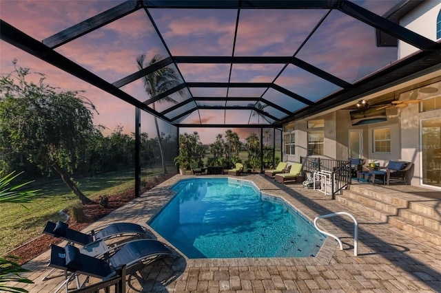 pool at dusk featuring a lanai, ceiling fan, a patio, and an outdoor hangout area