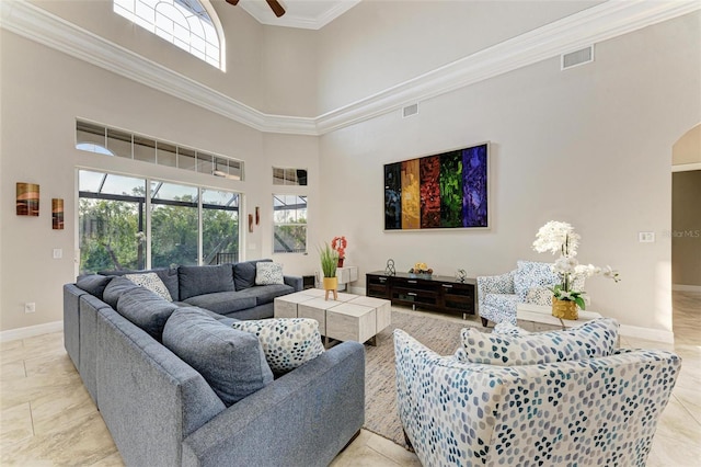 living room with a towering ceiling, plenty of natural light, ornamental molding, and ceiling fan