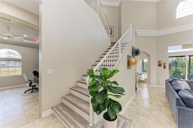 stairs with a towering ceiling, plenty of natural light, ornamental molding, and ceiling fan