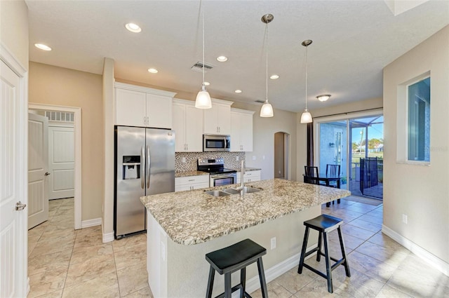 kitchen with sink, appliances with stainless steel finishes, an island with sink, decorative backsplash, and white cabinets