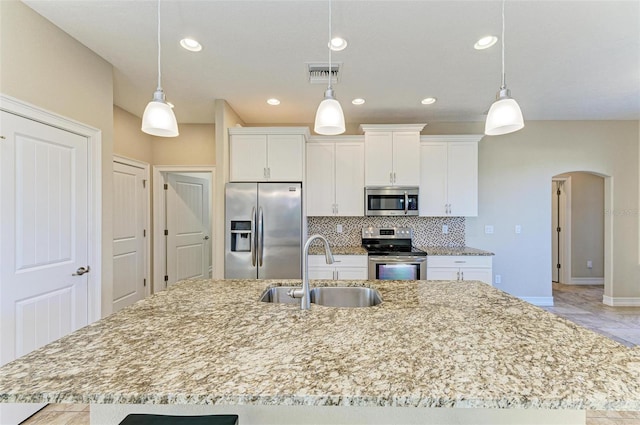 kitchen with sink, appliances with stainless steel finishes, hanging light fixtures, tasteful backsplash, and an island with sink