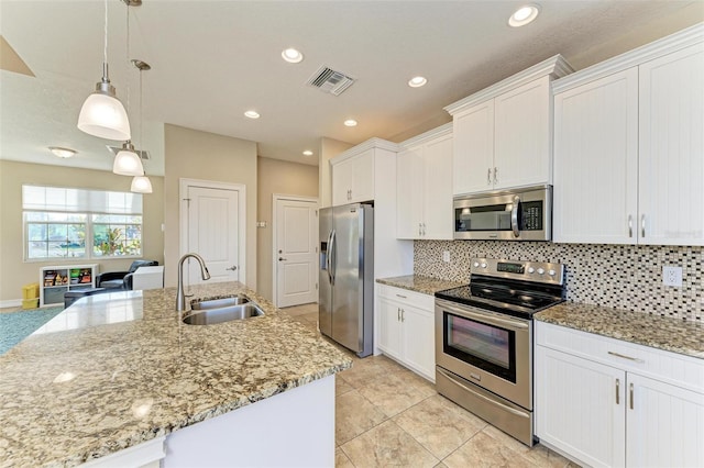 kitchen with appliances with stainless steel finishes, pendant lighting, sink, white cabinets, and a kitchen island with sink