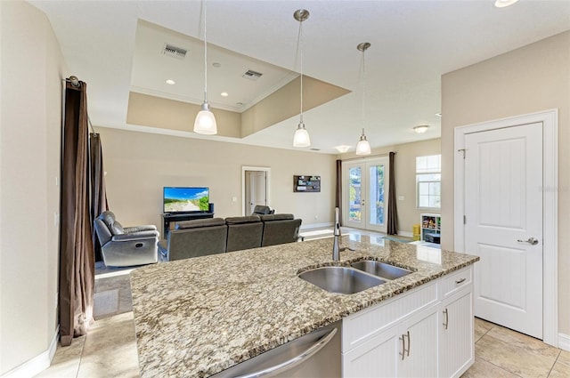 kitchen featuring white cabinetry, sink, hanging light fixtures, light stone countertops, and a center island with sink