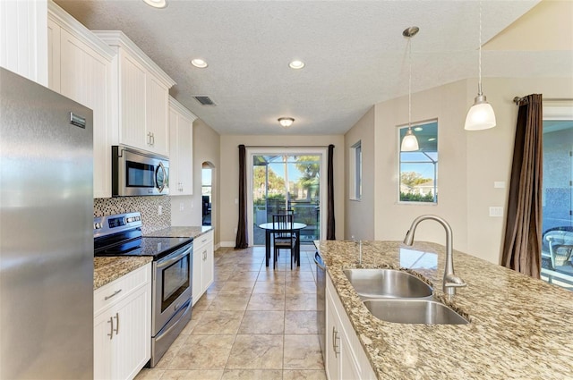 kitchen with pendant lighting, tasteful backsplash, sink, white cabinets, and stainless steel appliances