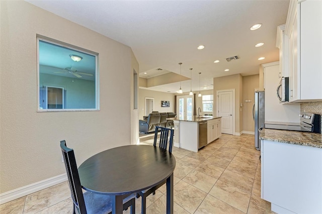 interior space with a kitchen island, white cabinetry, hanging light fixtures, stainless steel appliances, and light stone countertops