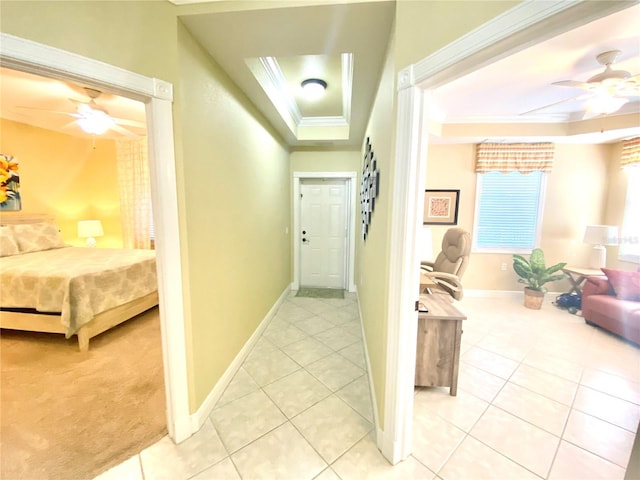 corridor with a raised ceiling, light tile patterned floors, baseboards, and ornamental molding