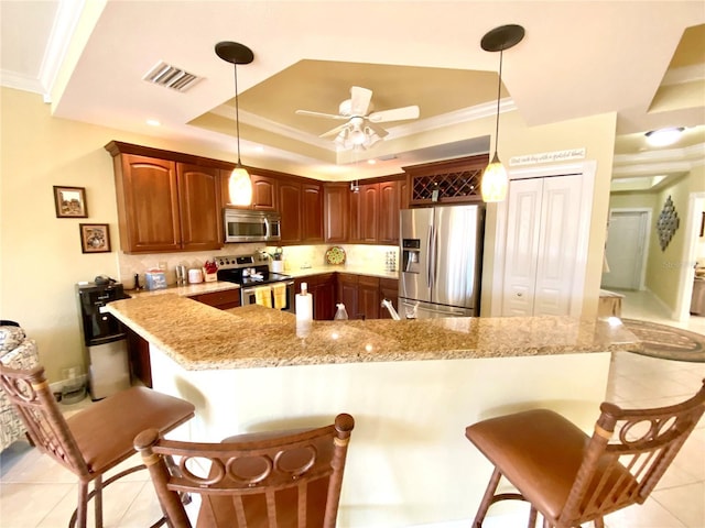 kitchen with stainless steel appliances, pendant lighting, a breakfast bar area, and a tray ceiling