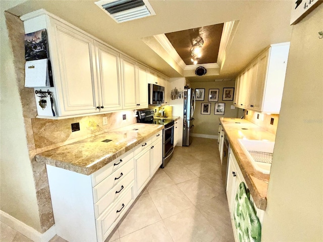 kitchen featuring white cabinets, a raised ceiling, sink, light tile patterned flooring, and stainless steel appliances