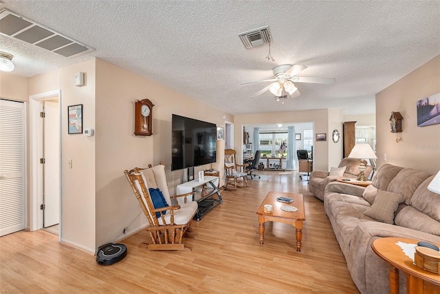 living room with ceiling fan, light wood-type flooring, and a textured ceiling