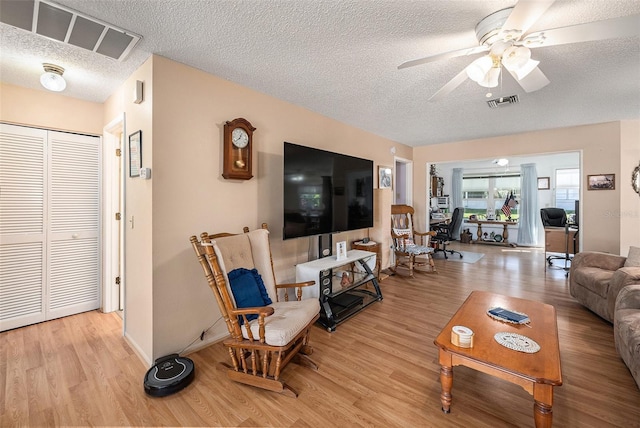 living room with ceiling fan, a textured ceiling, and light wood-type flooring