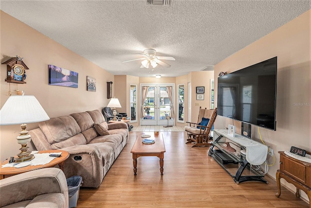 living room with french doors, light wood-type flooring, a textured ceiling, and ceiling fan