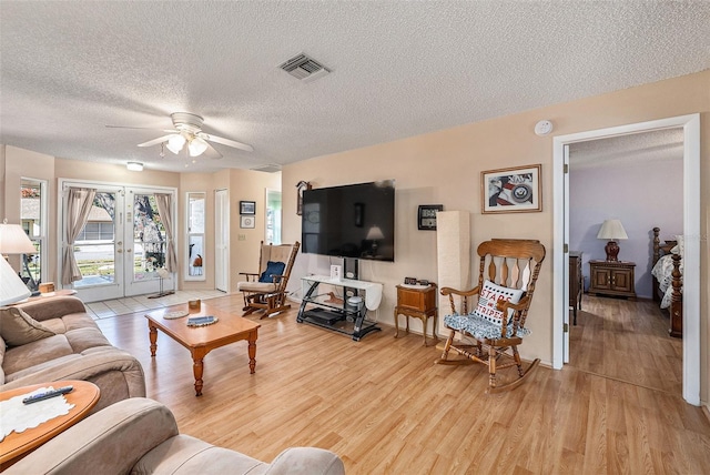 living room with ceiling fan, light hardwood / wood-style floors, a textured ceiling, and french doors