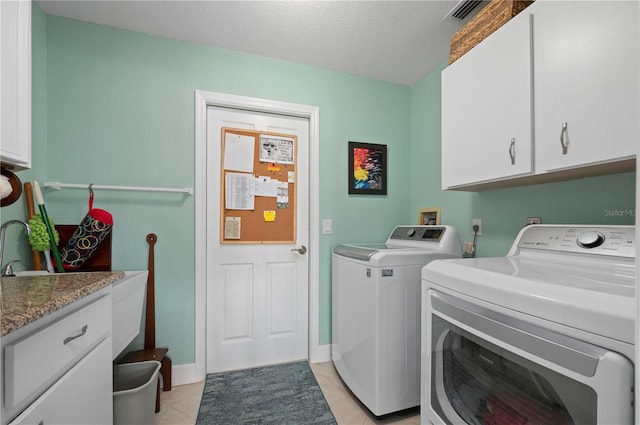 clothes washing area featuring washer and dryer, light tile patterned floors, a textured ceiling, and cabinets