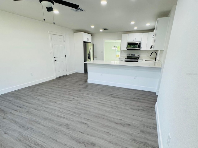 kitchen featuring kitchen peninsula, stainless steel appliances, ceiling fan, hardwood / wood-style floors, and white cabinetry