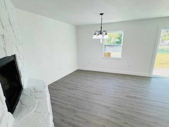 unfurnished dining area with a stone fireplace, dark hardwood / wood-style flooring, a healthy amount of sunlight, and an inviting chandelier