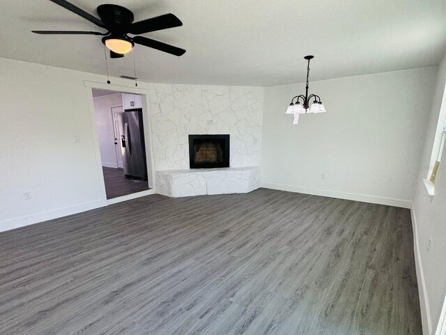 unfurnished living room featuring a fireplace, ceiling fan with notable chandelier, and dark hardwood / wood-style floors