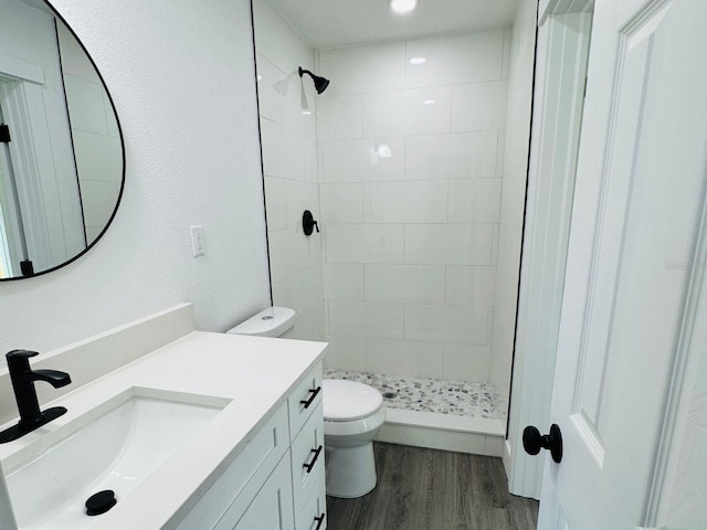 bathroom with tiled shower, vanity, wood-type flooring, and toilet