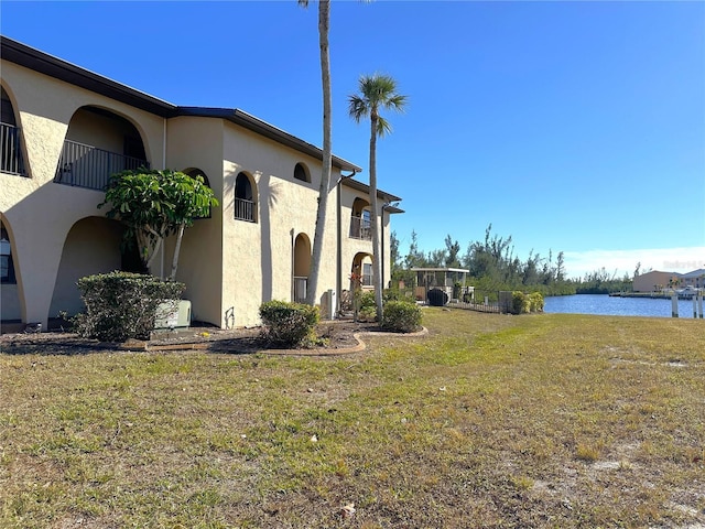 view of side of home featuring a water view, a lawn, a balcony, and stucco siding