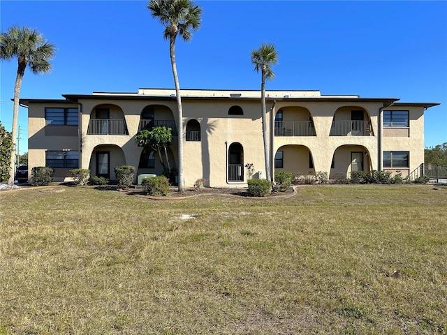 view of front of house featuring a balcony, stucco siding, and a front yard