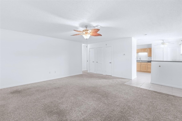 unfurnished living room featuring a textured ceiling, light colored carpet, a sink, a ceiling fan, and visible vents