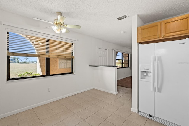 kitchen featuring white refrigerator with ice dispenser, light tile patterned floors, ceiling fan, light brown cabinetry, and a textured ceiling