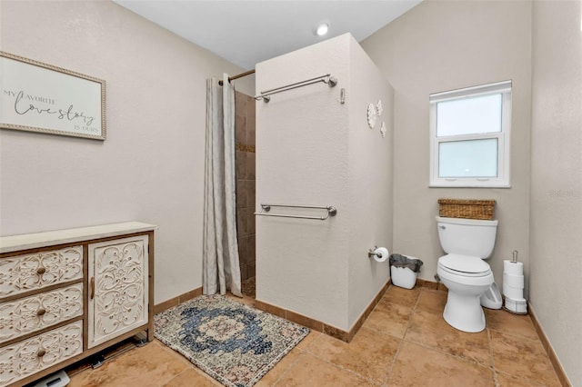 bathroom with a tile shower, toilet, and baseboards