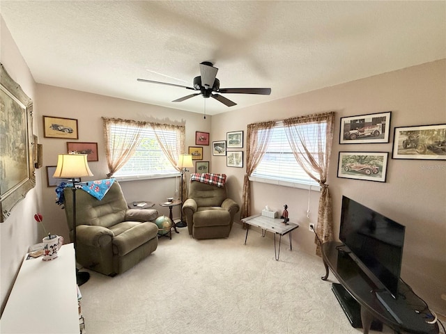 living area with a textured ceiling, light colored carpet, and ceiling fan