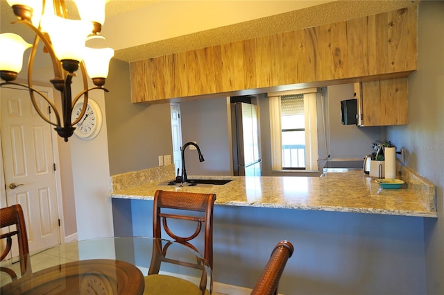 kitchen featuring kitchen peninsula, light stone countertops, sink, light tile patterned floors, and stainless steel refrigerator