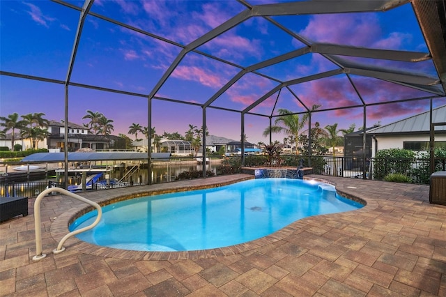 pool at dusk with pool water feature, a water view, glass enclosure, and a patio area