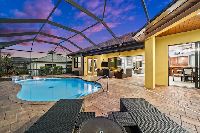 pool at dusk with a lanai, an outdoor living space, pool water feature, ceiling fan, and a patio area