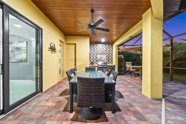 patio terrace at dusk featuring grilling area, ceiling fan, and a lanai