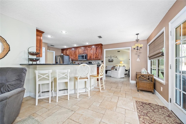 kitchen with pendant lighting, a kitchen bar, kitchen peninsula, stainless steel appliances, and a textured ceiling