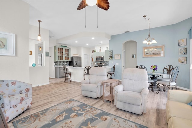 living room with ceiling fan with notable chandelier and light hardwood / wood-style floors