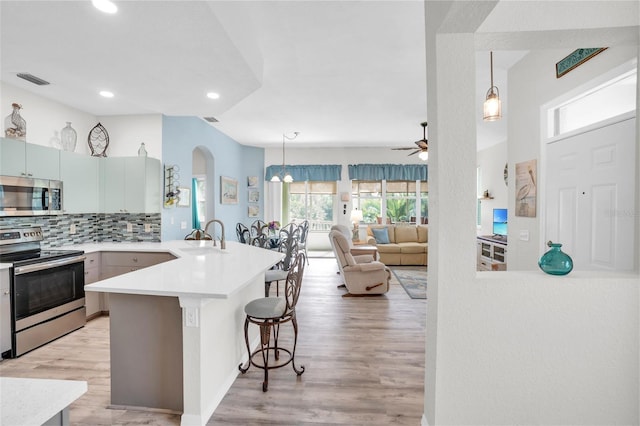 kitchen with kitchen peninsula, backsplash, a breakfast bar, stainless steel appliances, and pendant lighting