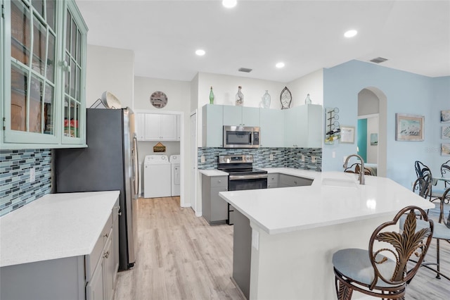 kitchen featuring a breakfast bar, sink, stainless steel appliances, kitchen peninsula, and washer and clothes dryer