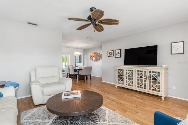 living room with ceiling fan with notable chandelier and light hardwood / wood-style floors