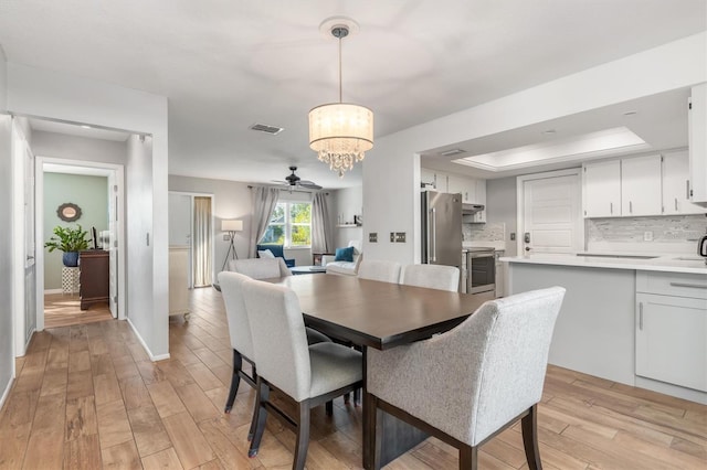 dining space featuring ceiling fan with notable chandelier, light hardwood / wood-style floors, and a tray ceiling