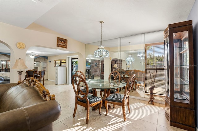 tiled dining space with ceiling fan with notable chandelier and vaulted ceiling