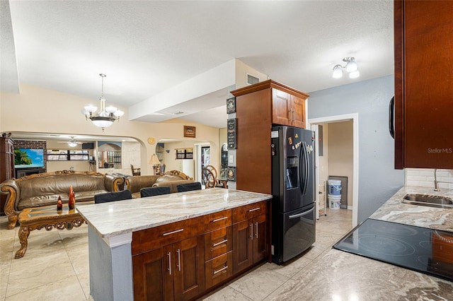 kitchen featuring backsplash, ceiling fan with notable chandelier, sink, stainless steel refrigerator with ice dispenser, and light stone countertops