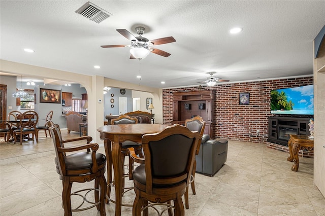 dining area with ceiling fan, a fireplace, brick wall, and a textured ceiling