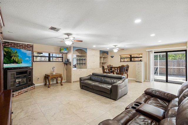 living room with a textured ceiling, a brick fireplace, and ceiling fan