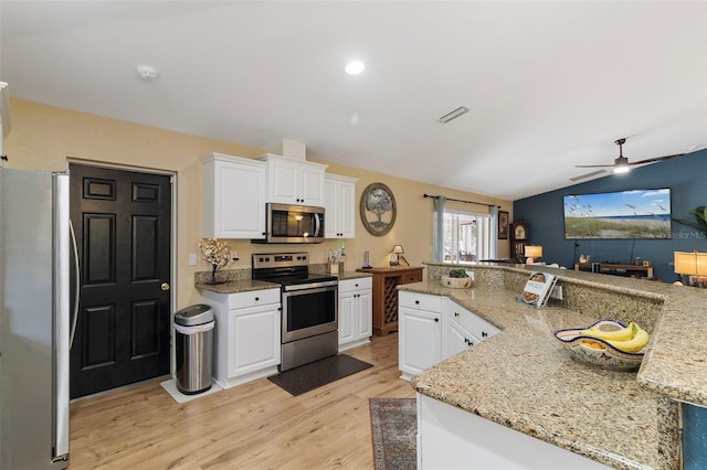 kitchen with lofted ceiling, white cabinets, light stone counters, and appliances with stainless steel finishes