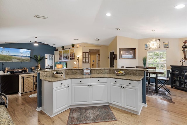 kitchen with lofted ceiling, white cabinetry, hanging light fixtures, and light hardwood / wood-style flooring