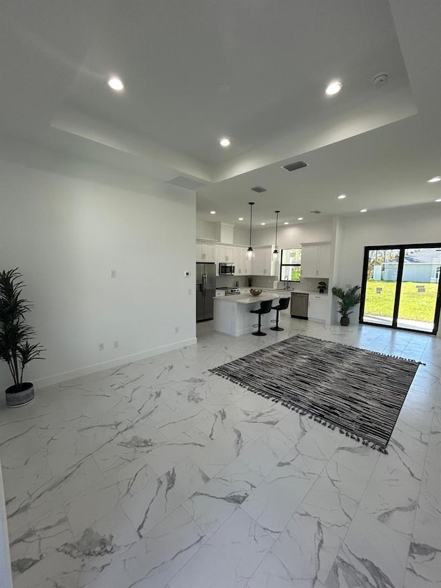 kitchen with decorative light fixtures, stainless steel appliances, white cabinetry, and a kitchen island