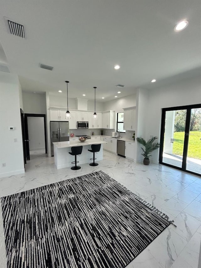 interior space with white cabinetry, pendant lighting, a kitchen island, and stainless steel appliances