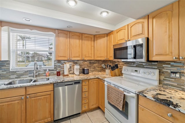 kitchen featuring appliances with stainless steel finishes, light tile patterned floors, light stone counters, decorative backsplash, and sink