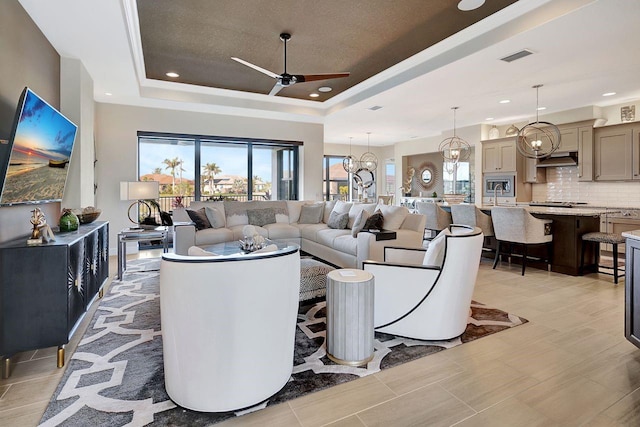 living room featuring ceiling fan with notable chandelier and a tray ceiling